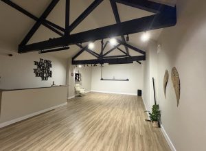 Empty studio with wood floors, black ceiling beams, and wall quote: It only takes one person to change your life you