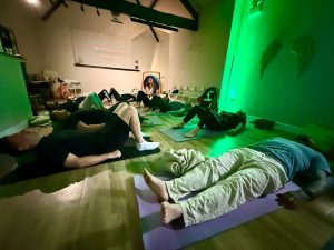 People lying on yoga mats in a studio with green lighting during a MAPPS MASTERY session