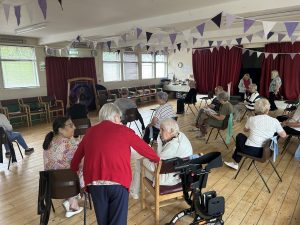 Seniors gathered and socializing in a community hall decorated with purple bunting