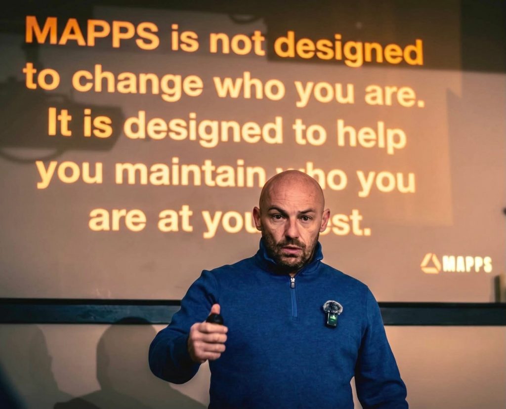 A man presents in front of a screen reading: MAPPS is not designed to change who you are. It is designed to help you maintain who you are at your best