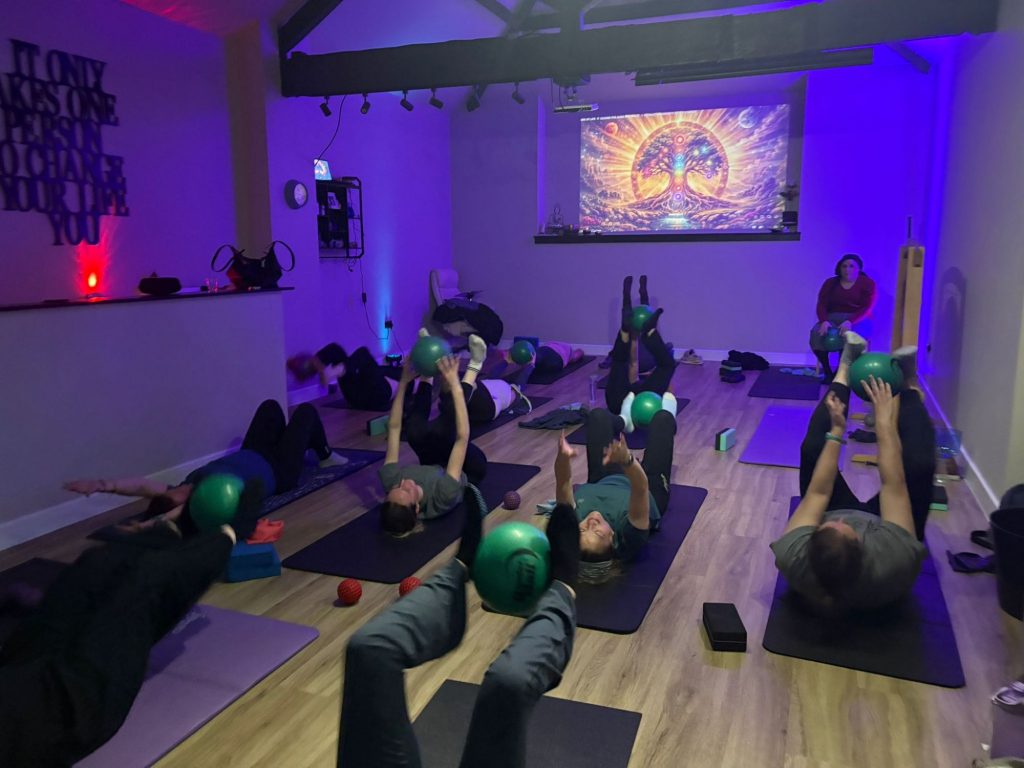 Lots of women lying down with green balls doing abs exercises during a Gong Pilates Class